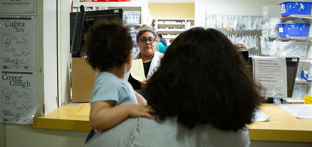Woman holding small child speaks to Pharmacist